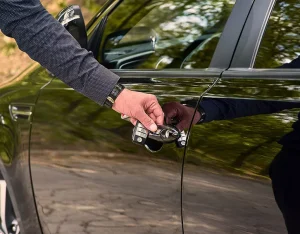 A person opening the door of a black car.